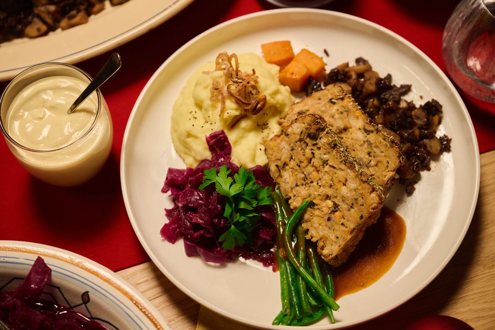 Eine Nahaufnahme eines Tellers mit Bratenstücken, Kartoffelstampf, Rotkohl und grünen Bohnen
