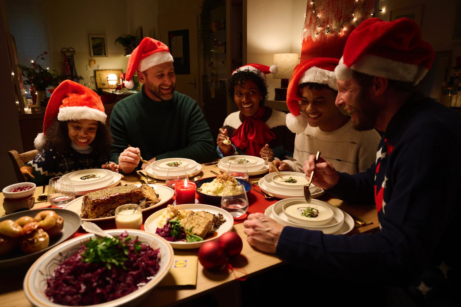 Eine Gruppe von Menschen mit Weihnachtsmützen lacht gemeinsam an einem reich gedeckten Festtagstisch