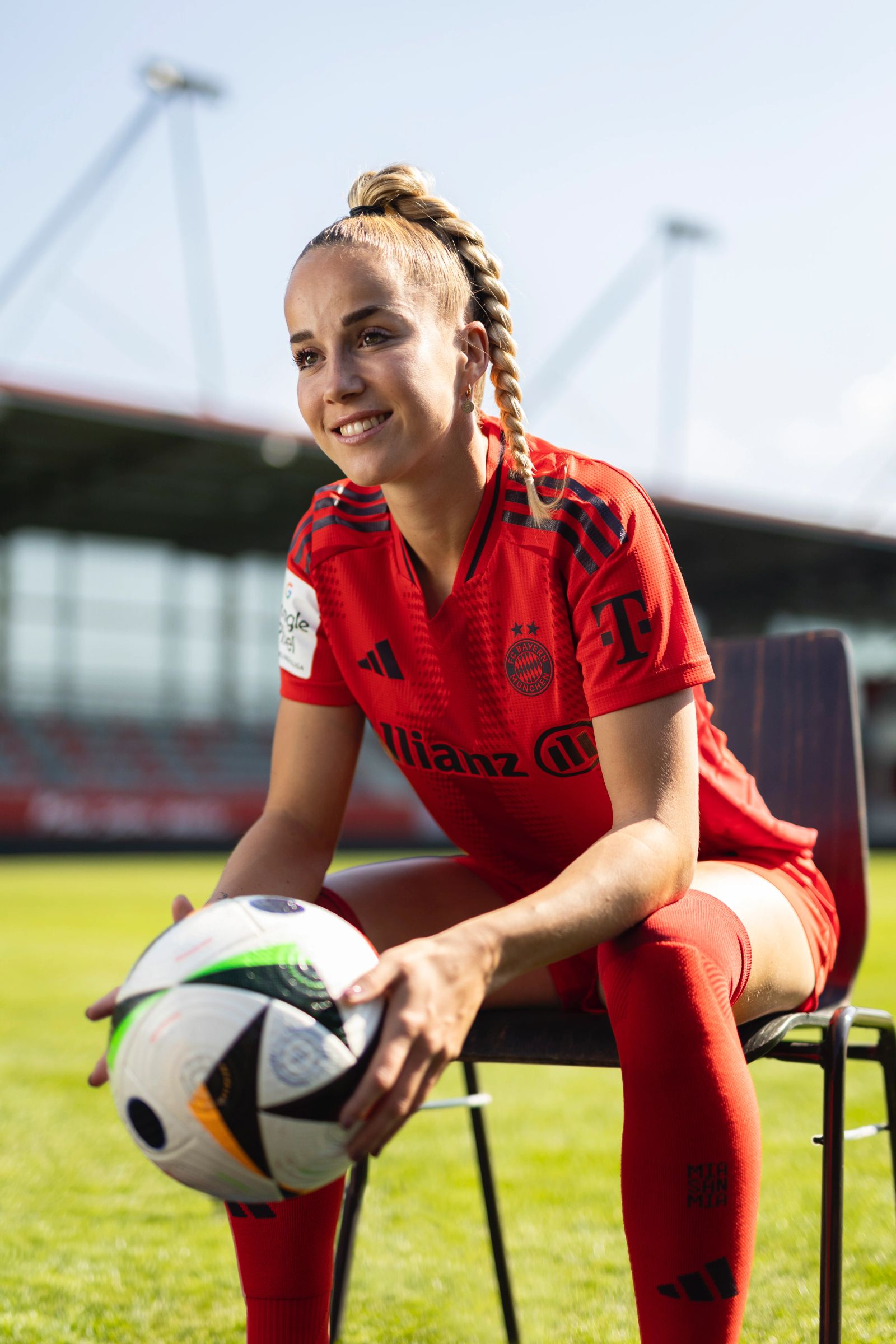 Porträt der Fußballspielerin Giulia Gwinn vom FC-Bayern-Muenchen im roten FC-Bayern-Trikot, sitzend mit einem Fußball auf einem Stuhl auf dem Spielfeld, fotografiert von Karl Scholten