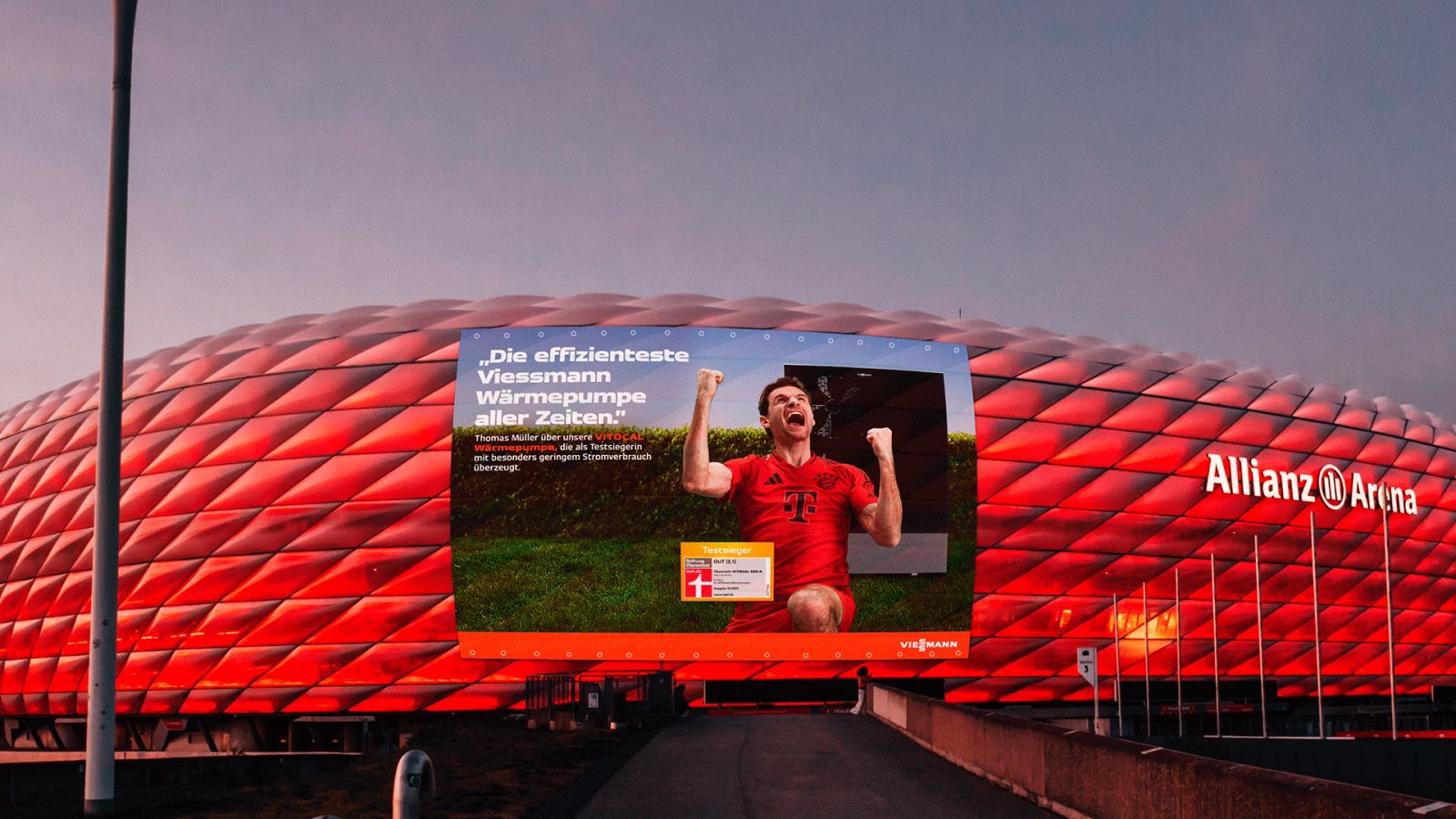 Ein von Karl Scholten fotografiertes Großplakat an der Allianz Arena zeigt FC Bayern-Star Thomas Müller in Siegerpose für eine Viessmann-Kampagne.