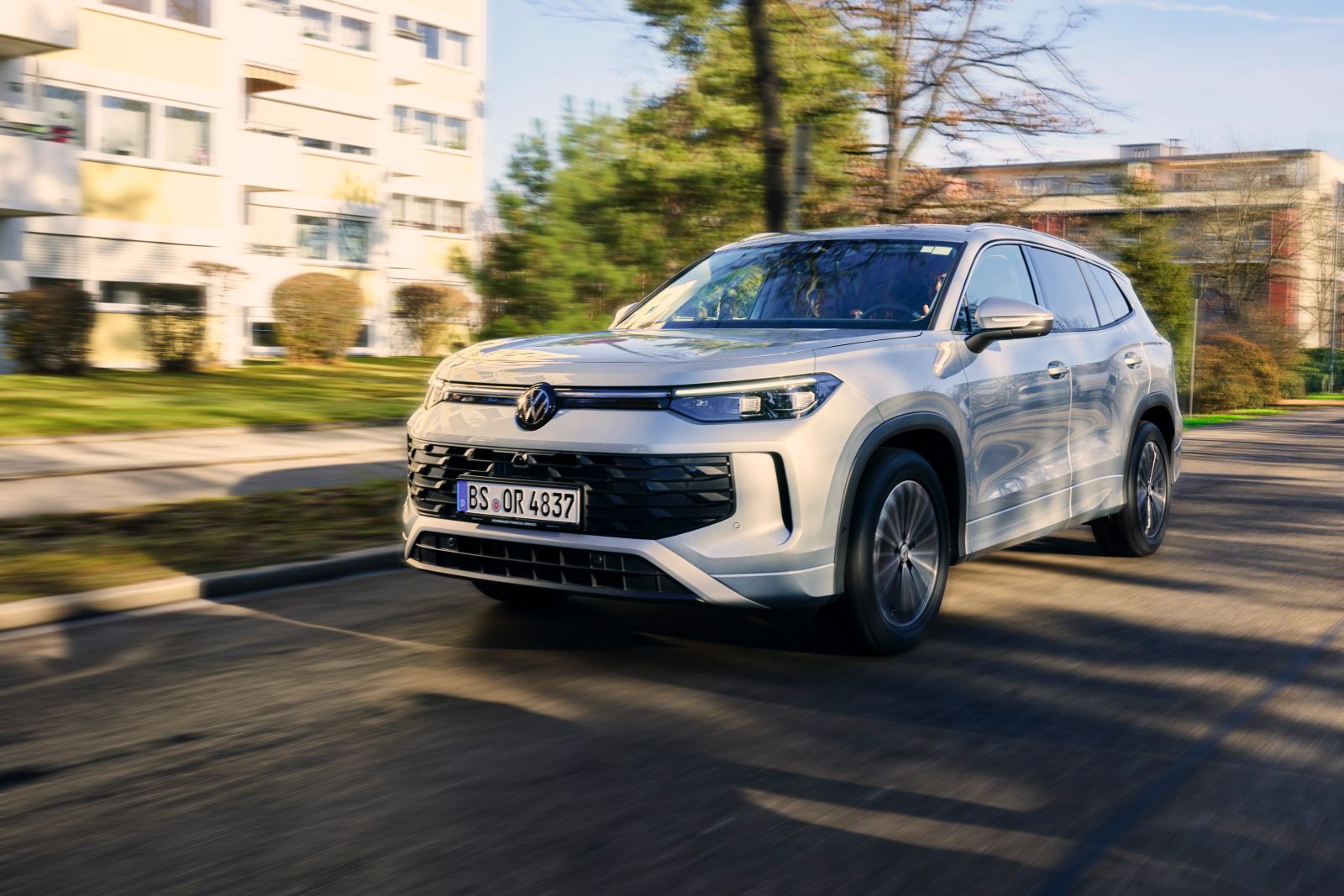 Ein silberner VW-SUV mit Continental-Reifen fährt dynamisch auf einer Straße vorbei an Wohngebäuden.