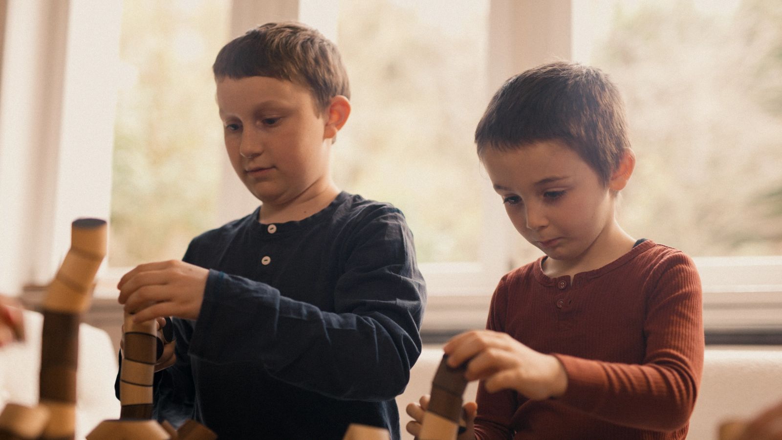 Zwei Kinder konzentrieren sich beim Bauen mit Holzspielzeug im Tageslicht