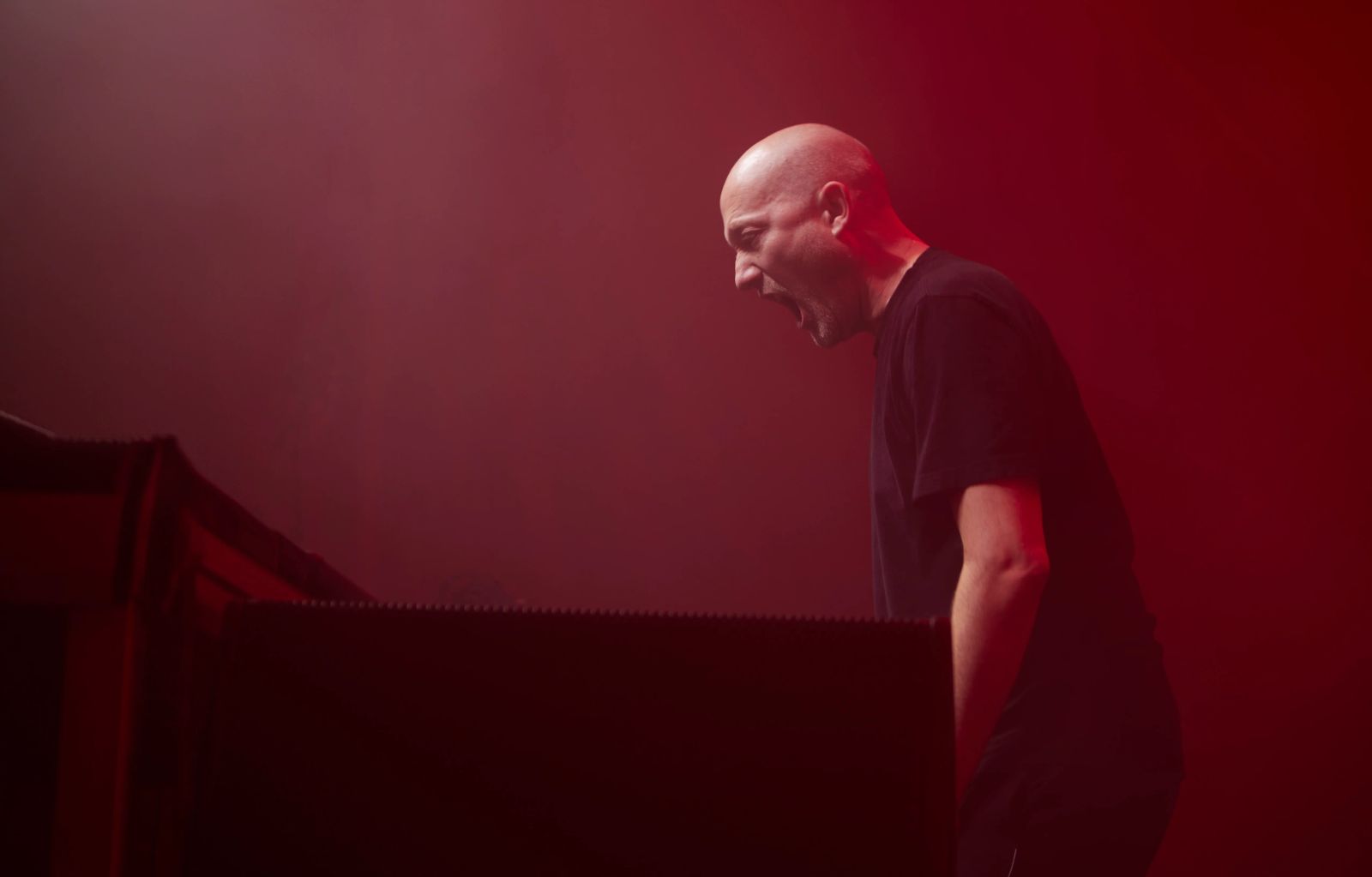 Paul Kalkbrenner steht auf der Bühne in rotem Licht und schreit