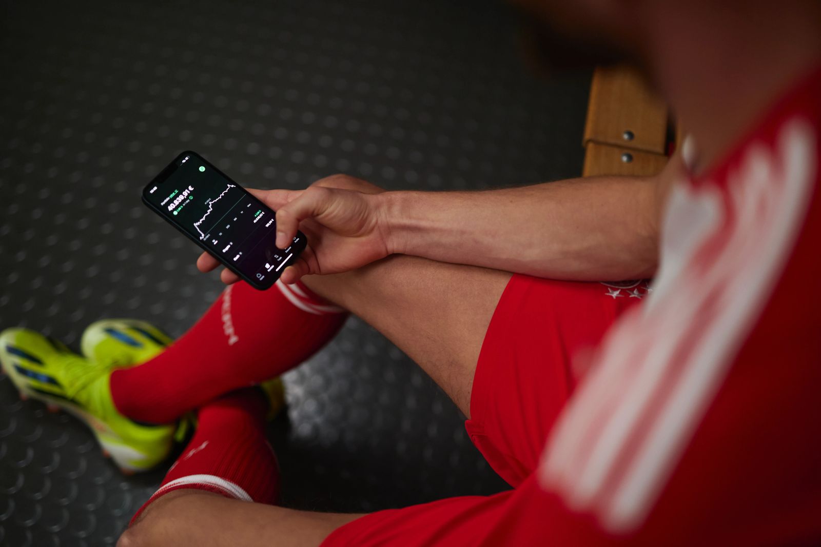 Detailaufnahme der Bitpanda-App auf einem Smartphone, gehalten von einem FC Bayern Spieler in den Kabinen der Allianz Arena, fotografiert von Karl Scholten.