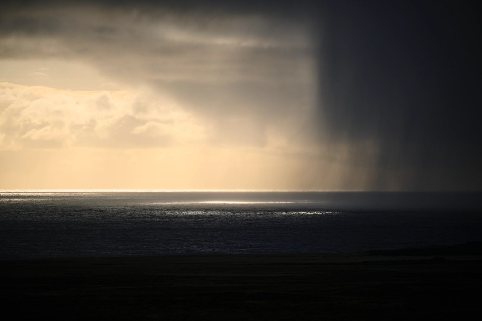 Ein dramatischer Regenschauer über dem glänzenden Meer an der isländischen Küste bei einfallendem Sonnenlicht, fotografiert von Karl Scholten.