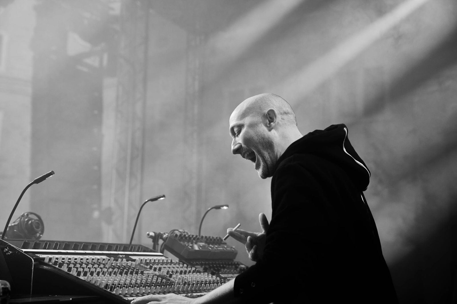 Paul Kalkbrenner steht auf der Bühne und und lacht vor seinem Mischpult