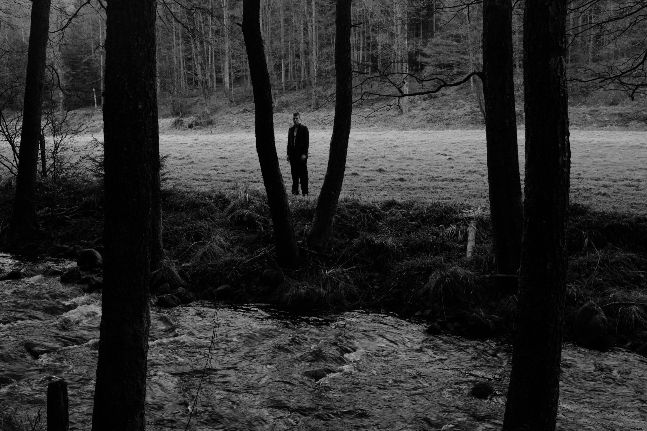 Schwarz-weiß Fashion Editorial im Schwarzwald: einsame männliche Figur in düsterer Waldlandschaft, fotografiert von Karl Scholten