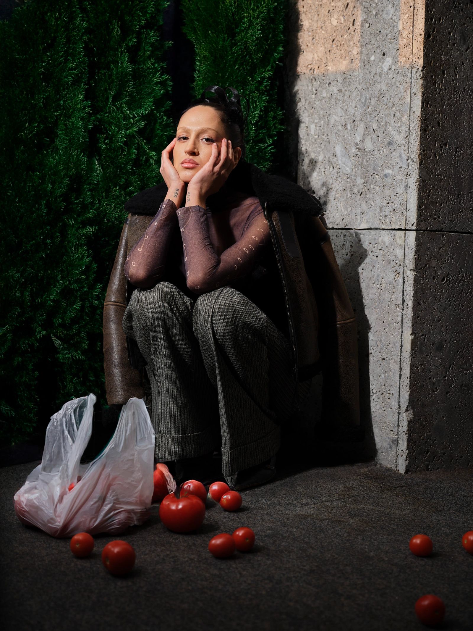 Hockende Frau mit Tomaten vor Betonwand im Editorial-Stil