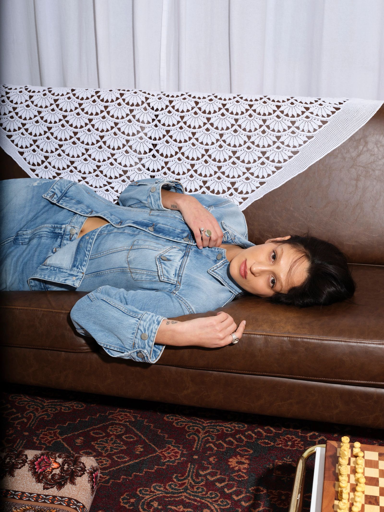 Frau liegt in Jeansoutfit sitzt auf einem Ledersofa