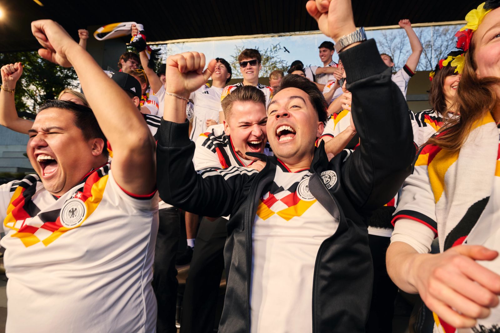Jubilierende deutsche Fußballfans auf einer Tribüne im Deutschland-Trikot mit Flaggen und Schals für die WM 2026