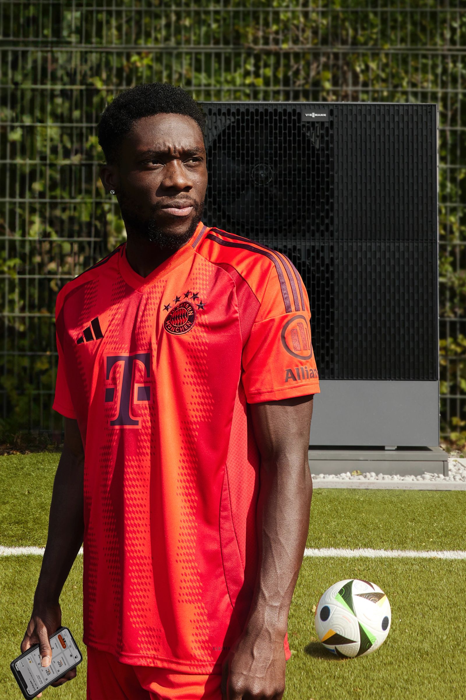 Alphonso Davies steht neben einer Wärmepumpe auf dem Rasen an der Säbener Straße