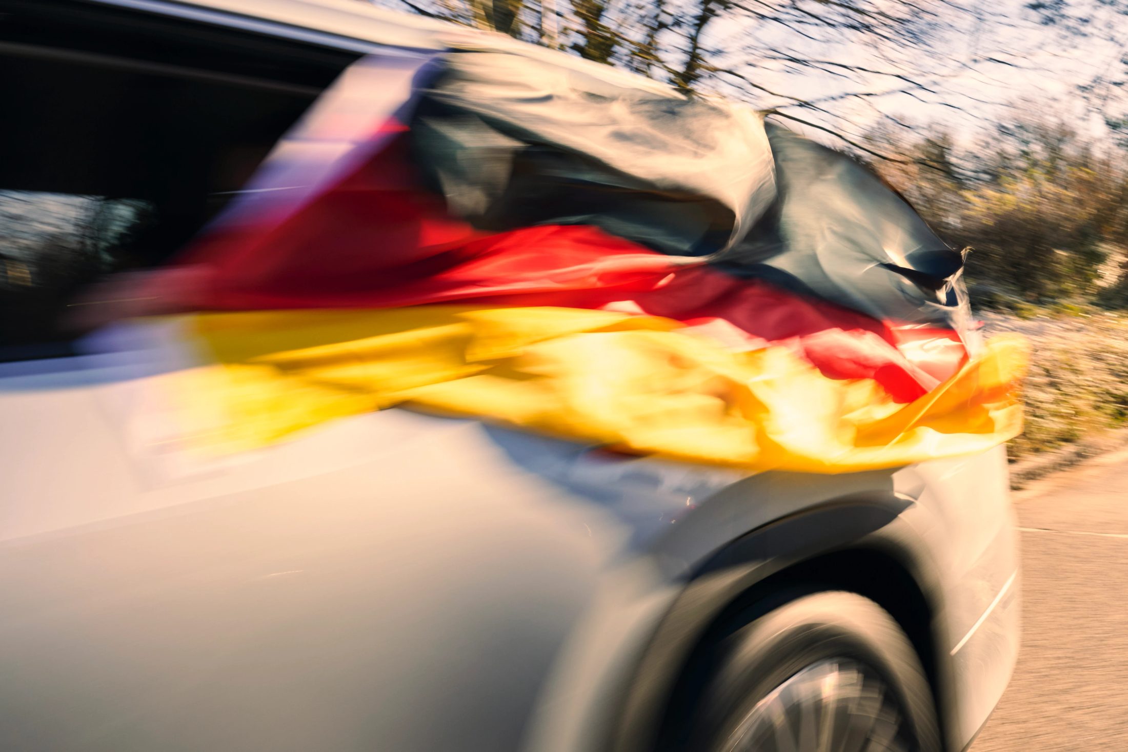 Dynamische Mitzieher-Aufnahme in voller Fahrt: Eine Deutschlandflagge weht aus dem Fenster eines weißen Autos