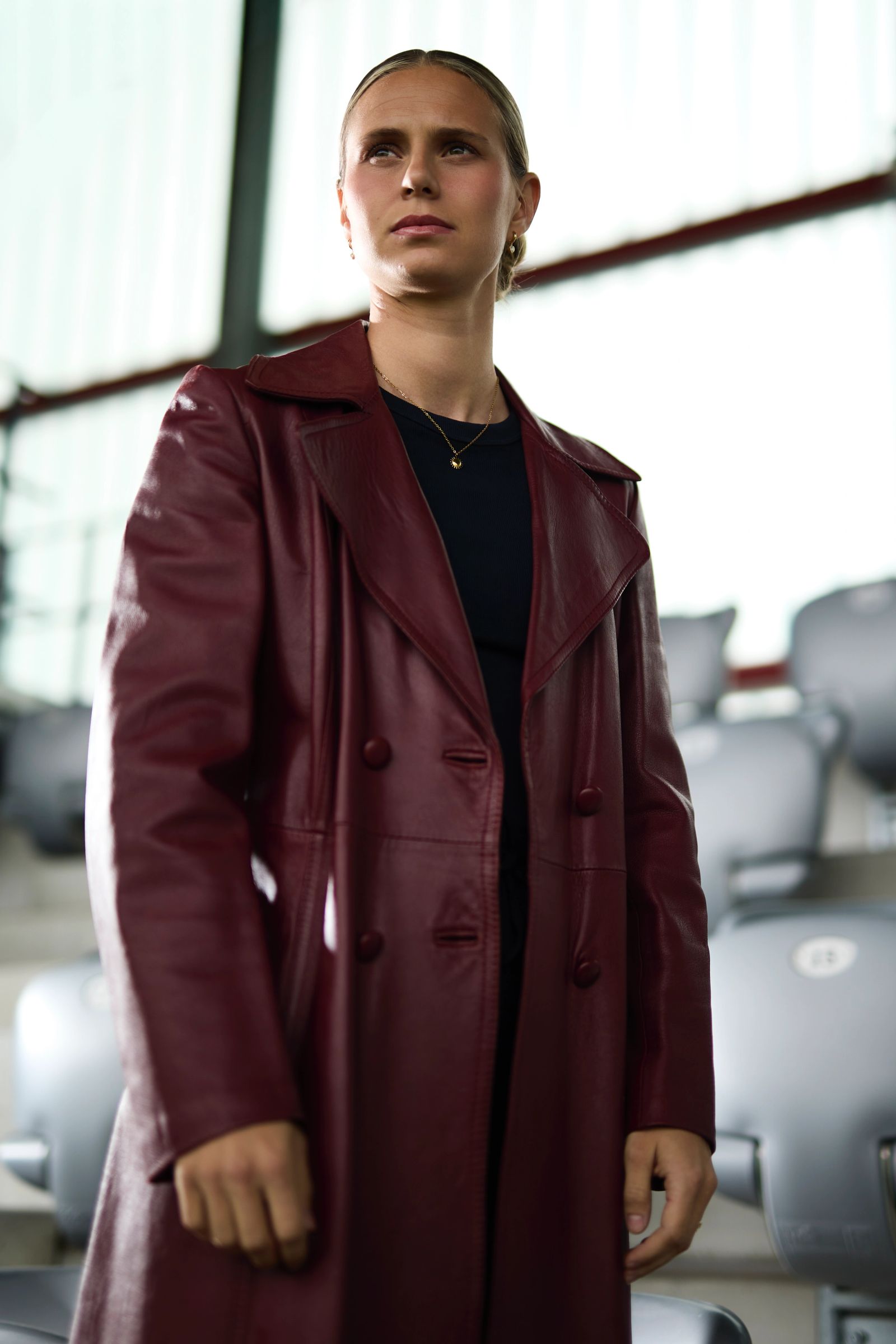 Fashion-Porträt von Klara Bühl in einem roten Ledermantel vor den Zuschauerrängen des Stadions, fotografiert von Karl Scholten.