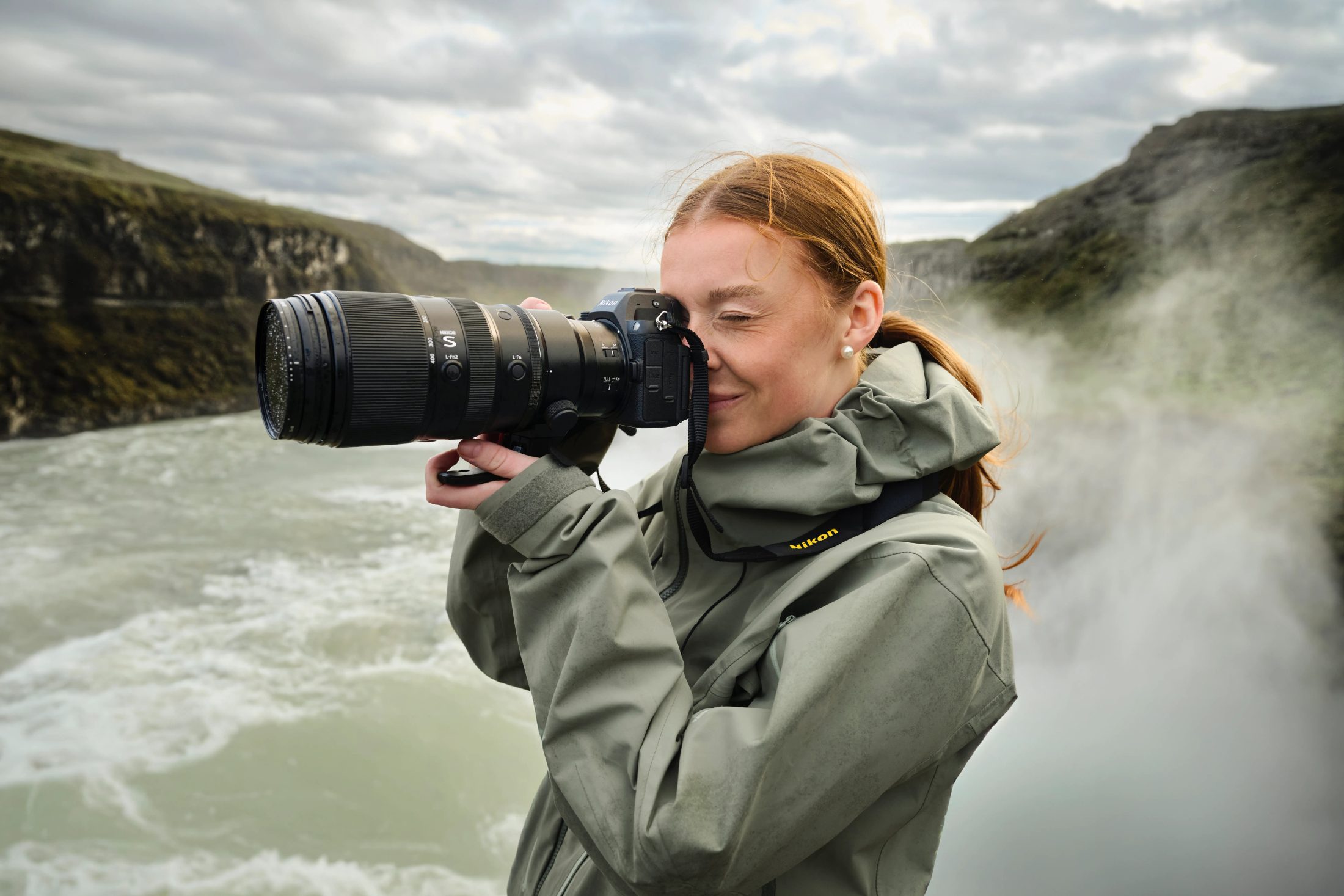 Eine junge Frau hält eine Nikon Z8 vor einem Wasserfall in Island