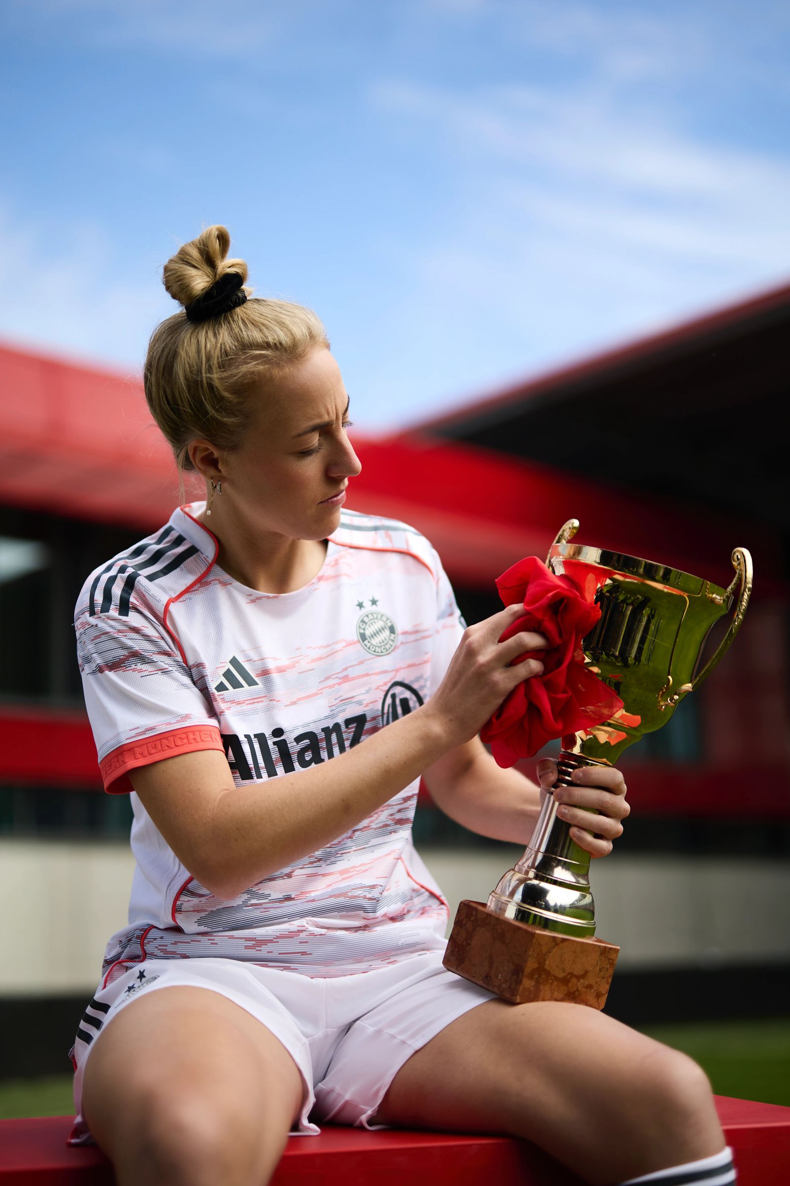 Porträt von FC Bayern Stürmerin Lea Schüller, die konzentriert eine goldene Trophäe mit einem roten Tuch poliert, fotografiert von Karl Scholten.