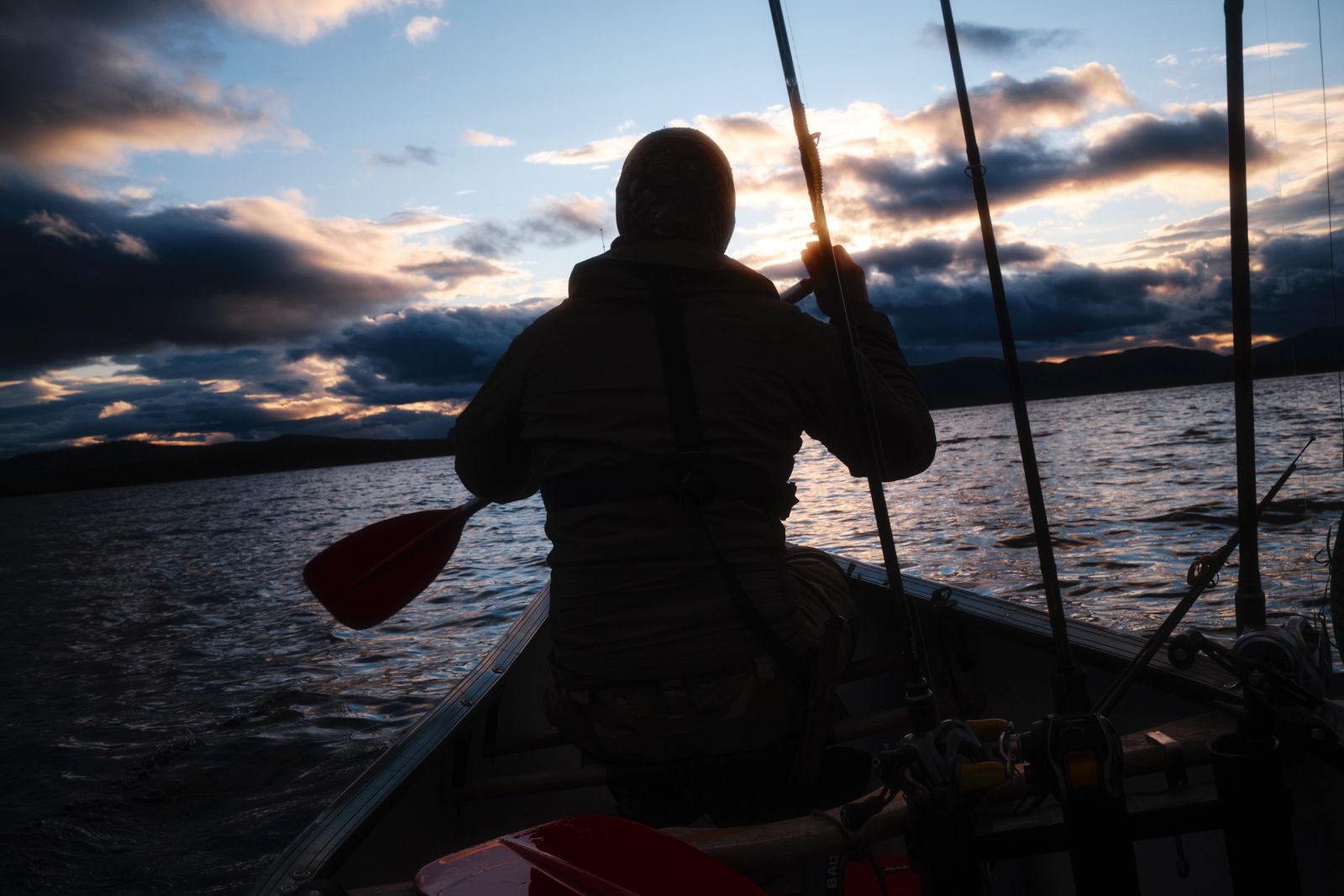 Kanufahrer paddelt bei Sonnenuntergang über einen weiten See mit Angelausrüstung an Bord.
