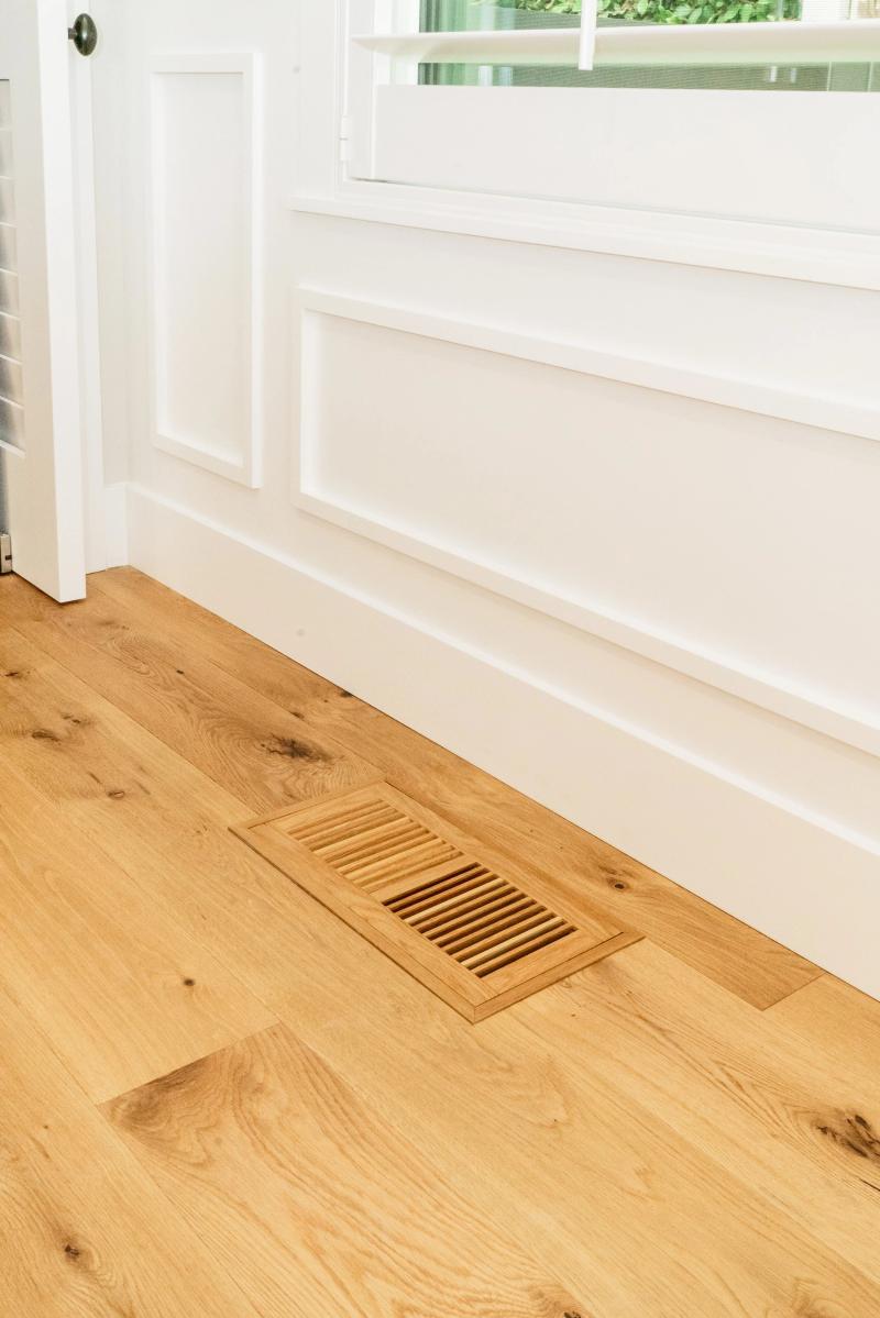Flush hardwood floor vent and clean baseboard detail showing preparation quality