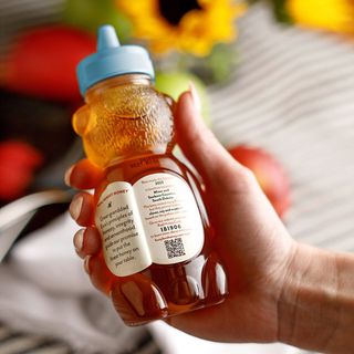 Person's arm holding a 12 OZ Busy Bee Raw USA Honey with the peel away