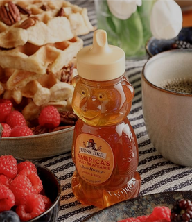 A bottle of busy bee honey next to some waffles, berries and coffee
