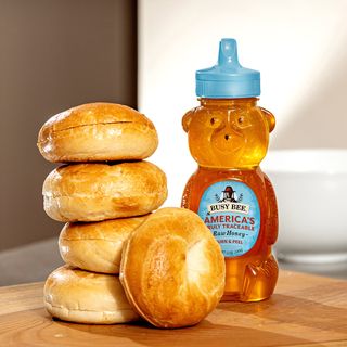 12 OZ Busy Bee Raw USA Honey bottle on table next to 5 stacked beagles