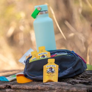 9 OZ RAW USA HONEY TO GO couple of single serve pouches in the field next to a bottle of water