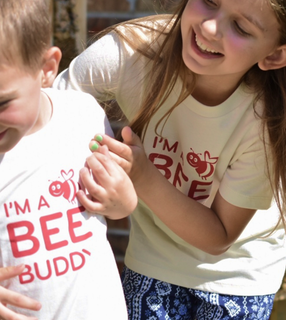 Two children in "I'm a bee budy" themed shirts, a boy and a girl, are smiling and playing.
