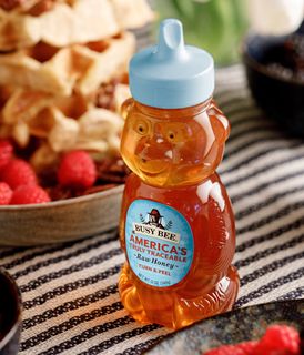 A bottle of busy bee honey next to some waffles, berries and coffee