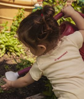 A child in a "BEESPONSIBLE" shirt waters plants in a garden.