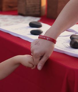 A child's hand and adult hand, both sporting red Beesponsible temporary tattoos