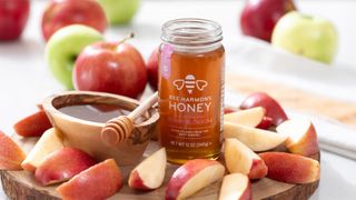 Honey jar and dipper with sliced apples on a wooden board.