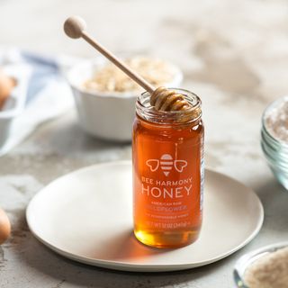 Jar of Bee Harmony Wildflower Honey with a honey dipper resting inside, placed on a plate.