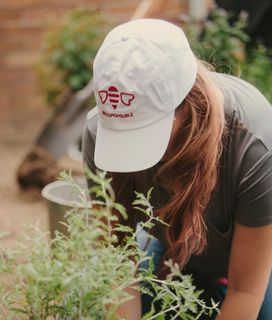 Woman wearing a white Beesponsible hat plants flowers in a garden