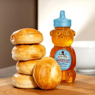 12 OZ Busy Bee Raw USA Honey bottle on table next to 5 stacked beagles