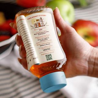 16 oz Raw USA Honey bottled hold by person reading bottle with peel away
