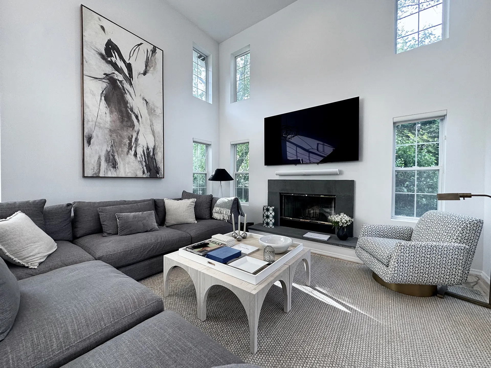 A SEASONAL residence living room, gray sectional sofa facing a fireplace beneath abstract art