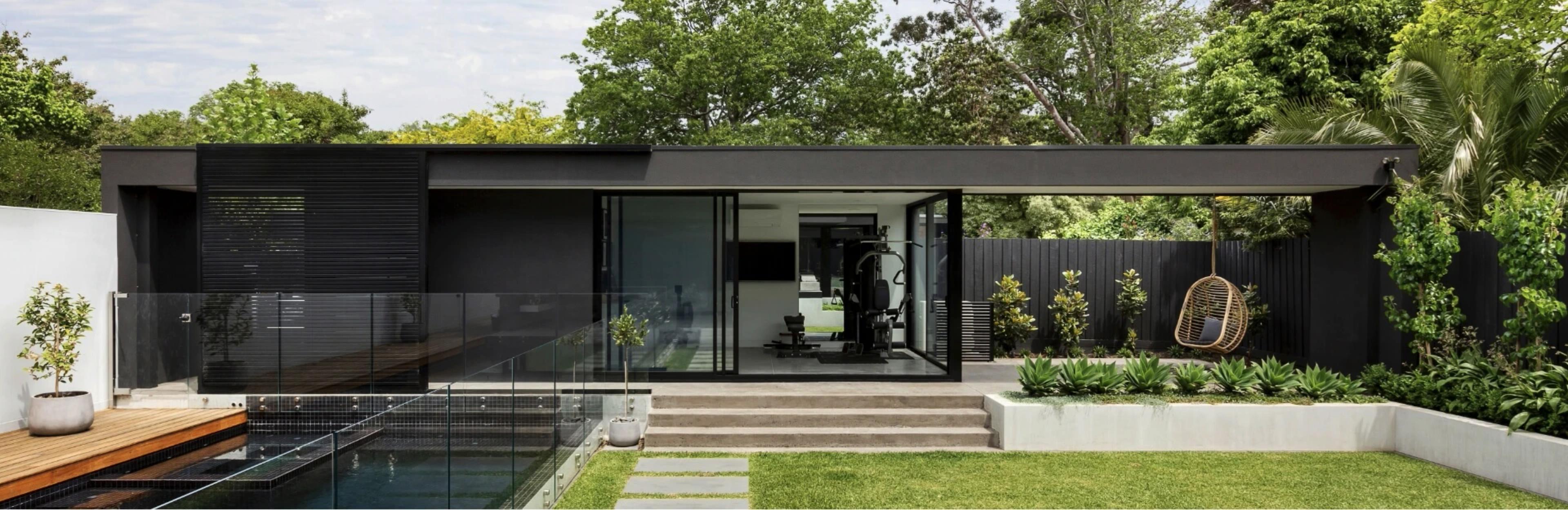 View of a backyard with a green lawn, glass fenced pool and seperate structure.