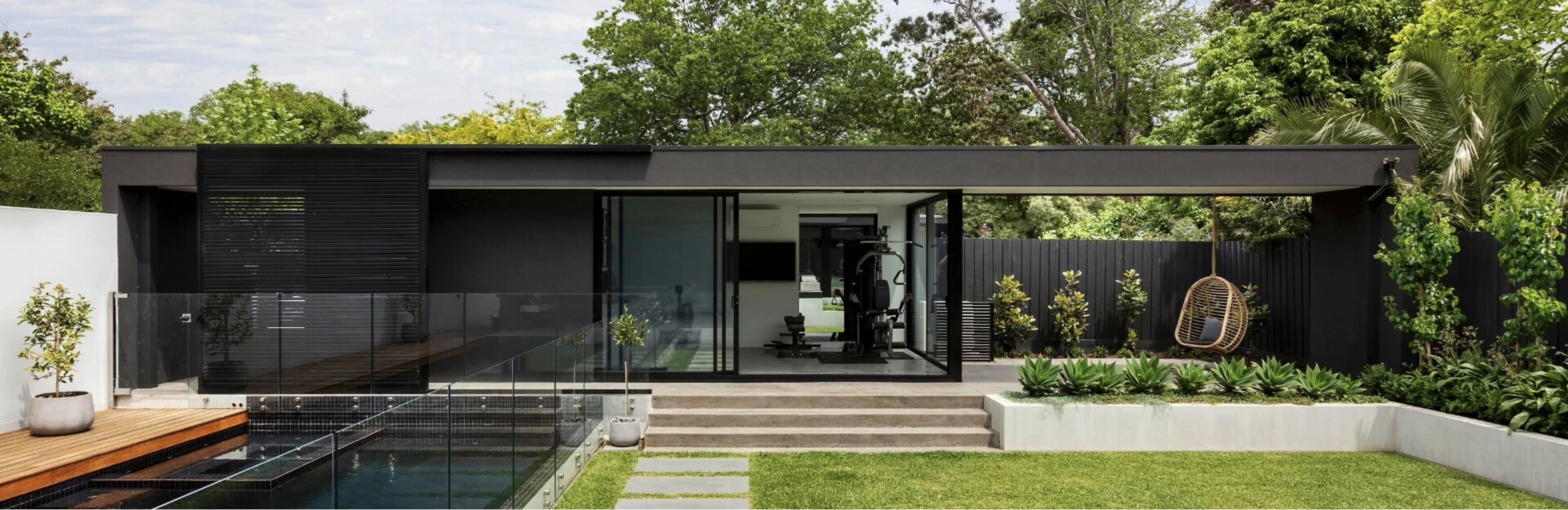 View of a backyard with a green lawn, glass fenced pool and seperate structure.