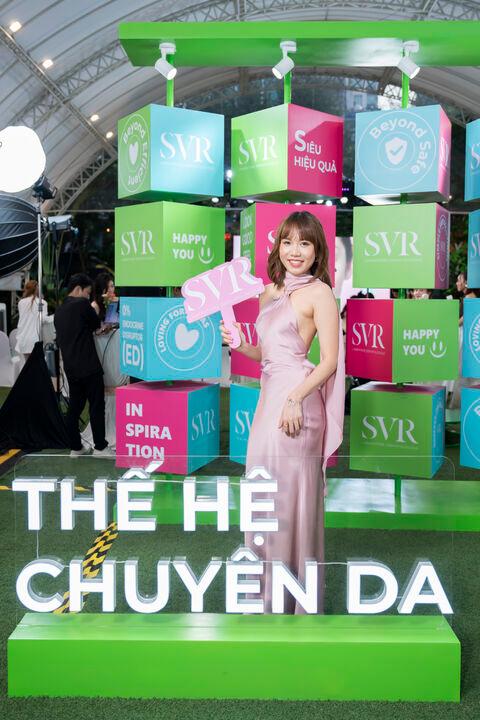 A smiling woman in a pink satin dress holds a pink SVR sign in front of colorful SVR branded blocks at an event.