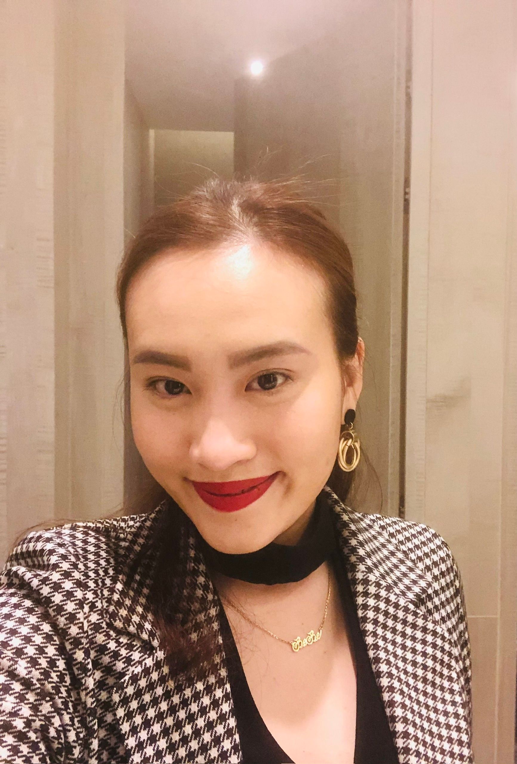 Smiling woman with long brown hair, wearing a dark blazer and a gold finger ring.