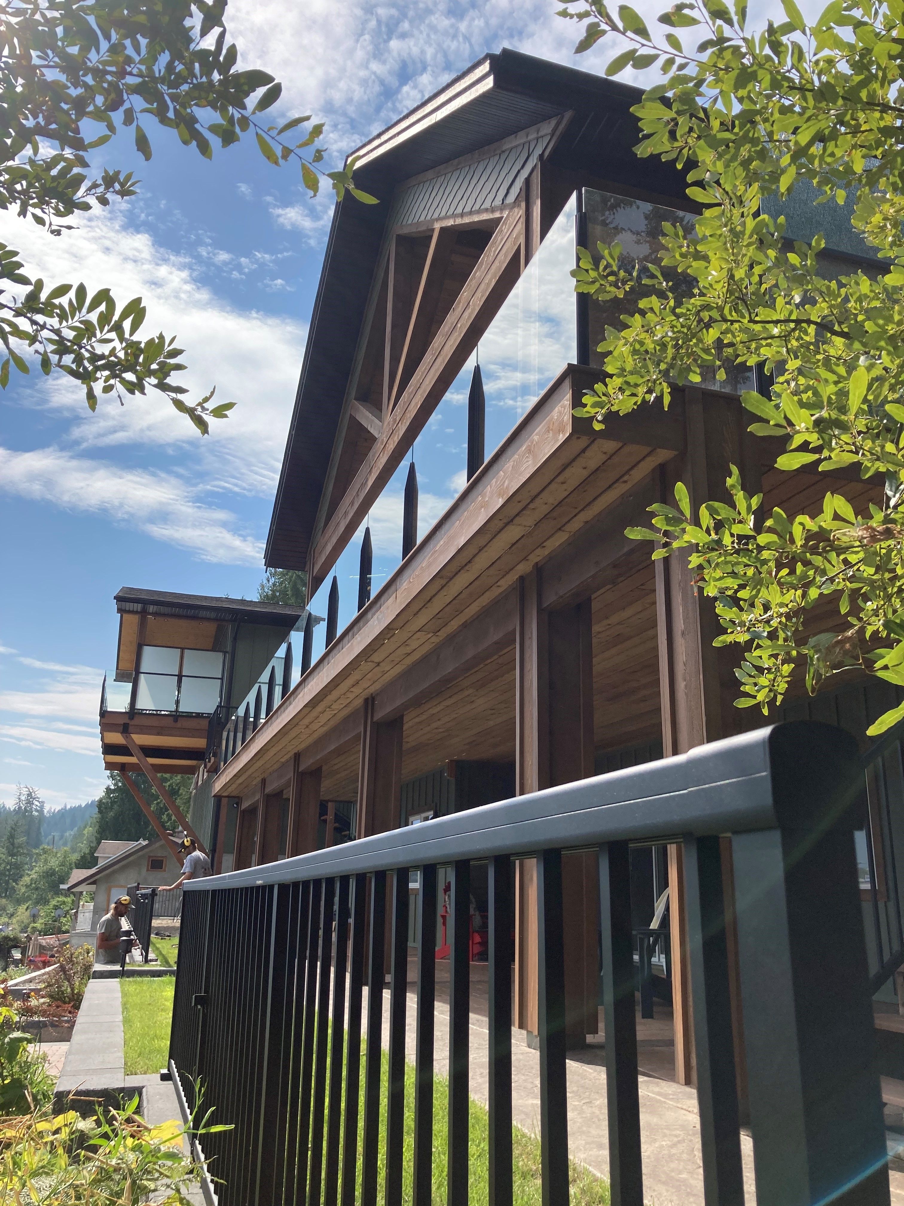 Two-storey timber frame home in Christina Lake, BC featuring black aluminum picket railing on the lower level and frameless infinity glass railing on the upper balcony