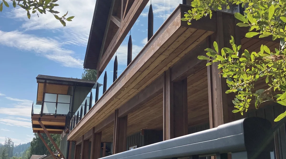 Two-storey timber frame home in Christina Lake, BC featuring black aluminum picket railing on the lower level and frameless infinity glass railing on the upper balcony