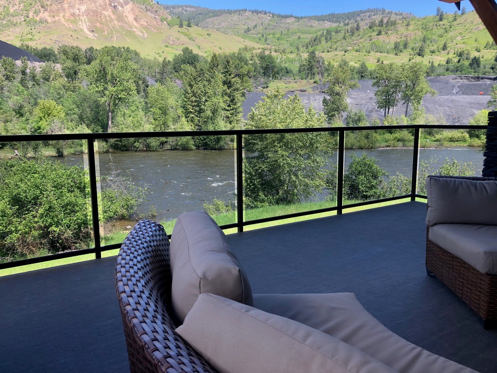 Fascia mount glass component railing with black aluminum frame on a waterfront deck in Rossland BC with river views and outdoor lounge furniture