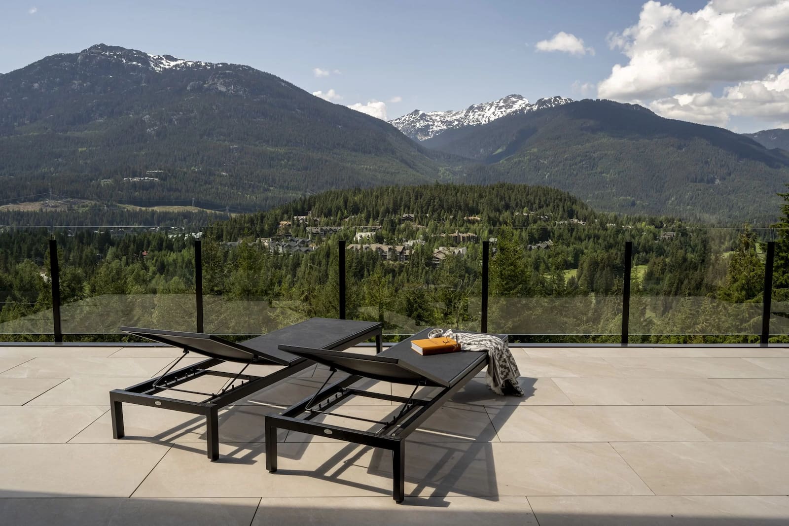 Frameless topless glass railing on a luxury Whistler BC deck with lounge chairs and unobstructed mountain views
