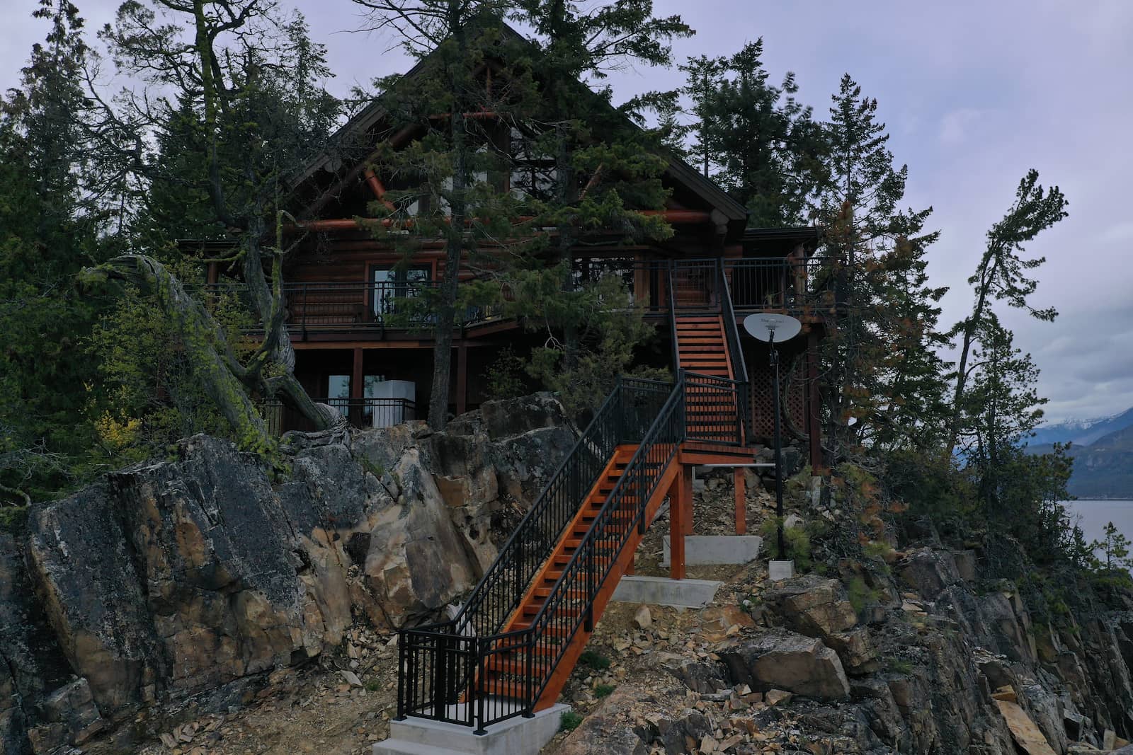 Textured black aluminum picket stair railing with gate on a multi-level timber frame home built on natural rock terrain in Christina Lake BC