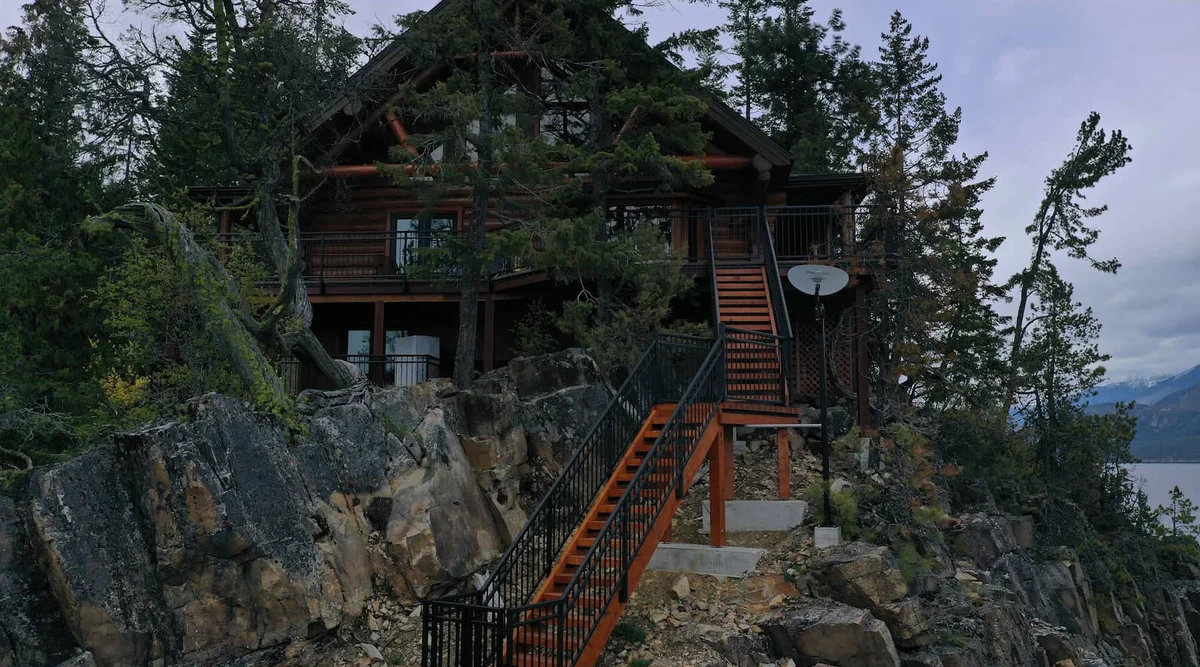 Textured black aluminum picket stair railing with gate on a multi-level timber frame home built on natural rock terrain in Christina Lake BC