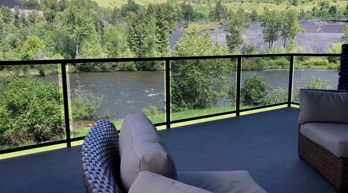 Glass component railing with black aluminum frame on a waterfront deck in Rossland, BC overlooking a river with outdoor lounge furniture