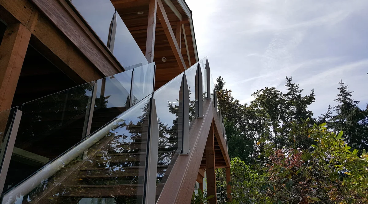 Frameless topless glass railing on exterior stairs of a timber frame home viewed from below showing glass panels in aluminum post channelsFrameless topless glass railing on exterior stairs of a timber frame home viewed from below showing glass panels in aluminum post channels