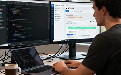 Developer working with AI coding assistant on dual monitors showing code and AI interface