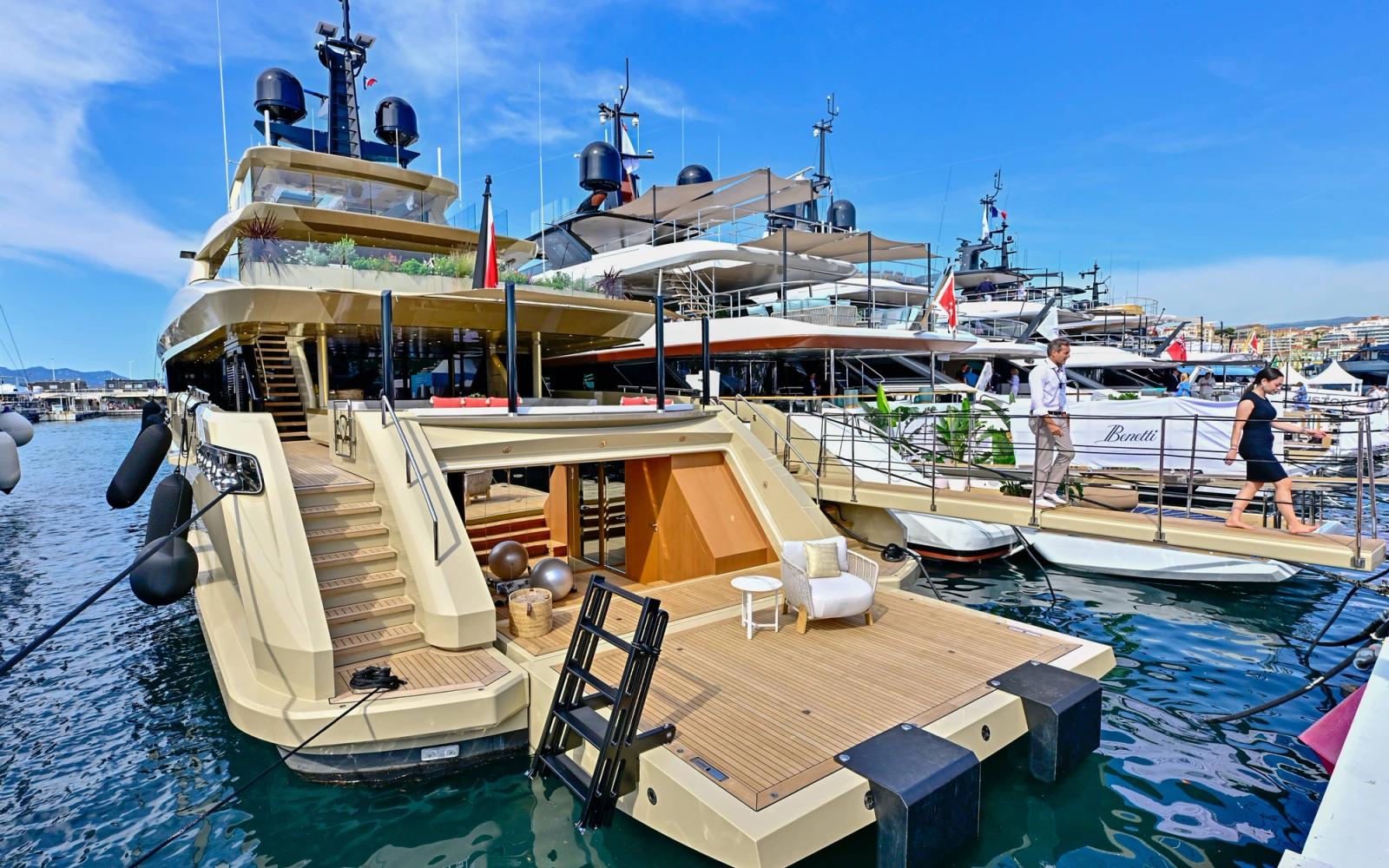 Luxury yacht docked at a marina with calm waters and a clear sky.