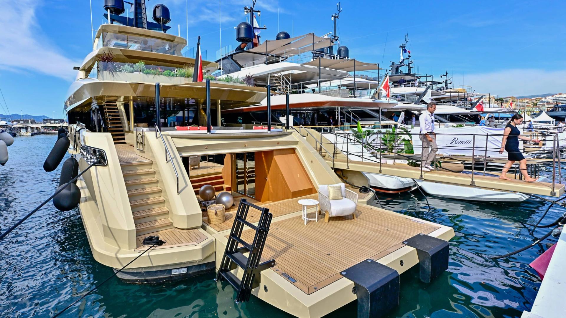 Luxury yacht docked at a marina with calm waters and a clear sky.